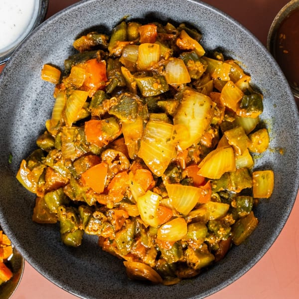 Close-up of a vibrant Indian vegetable dish with okra, onions, and spices in a dark bowl.