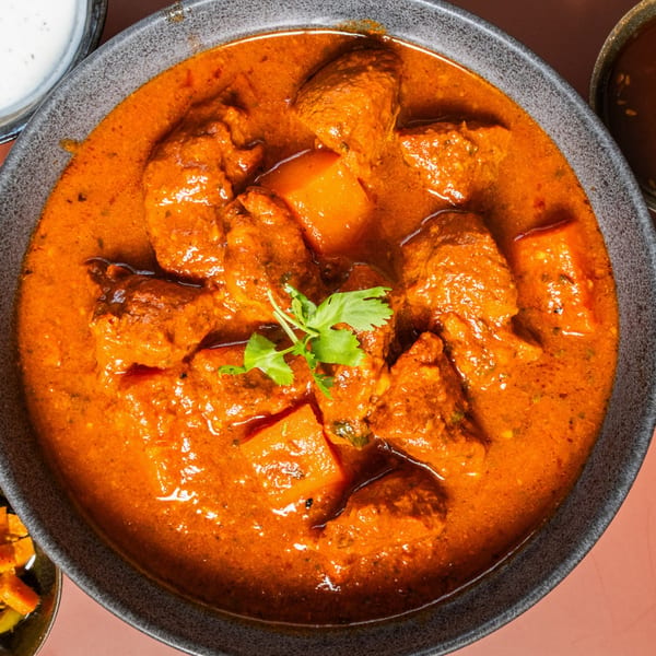 Close-up of a vibrant orange Indian curry with chicken and potatoes, garnished with fresh cilantro.