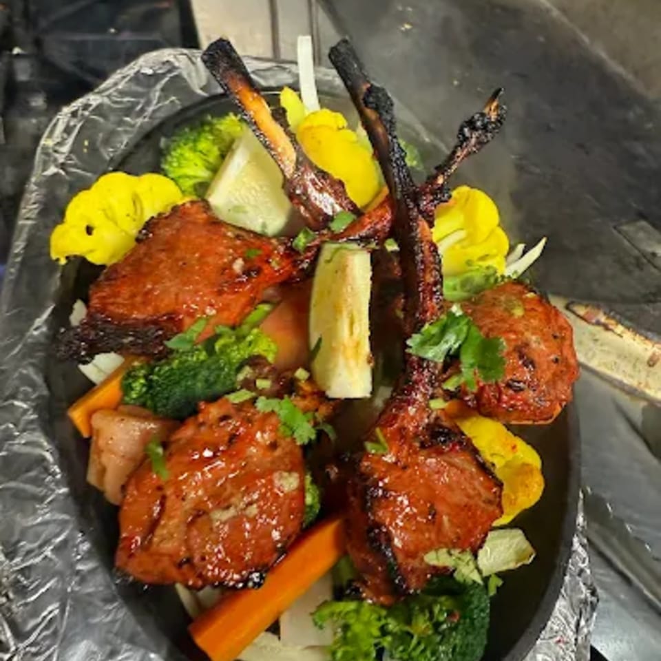 Indian Tandoori lamb chops and chicken tikka with vegetables on a sizzling platter.