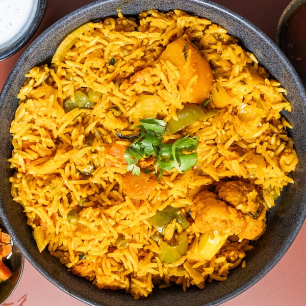 Close-up of Indian vegetable biryani with rice, cauliflower, bell peppers, and cilantro in a dark bowl.