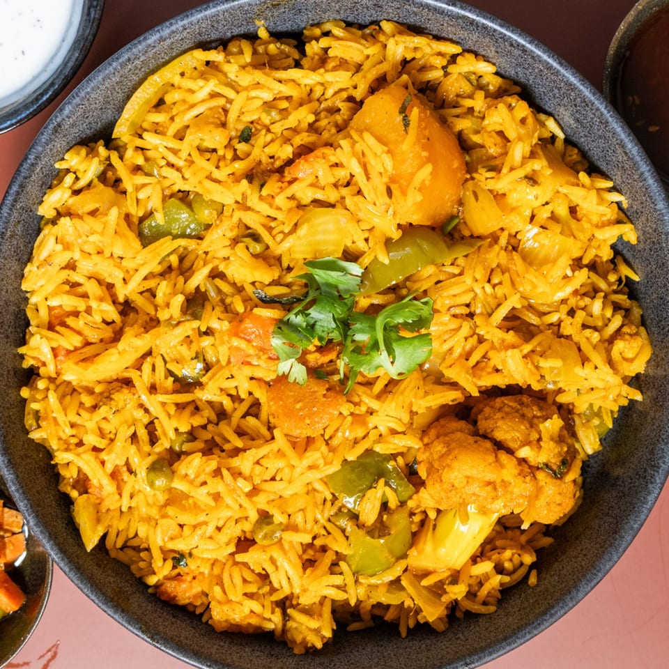 Close-up of Indian vegetable biryani with rice, cauliflower, bell peppers, and cilantro in a dark bowl.