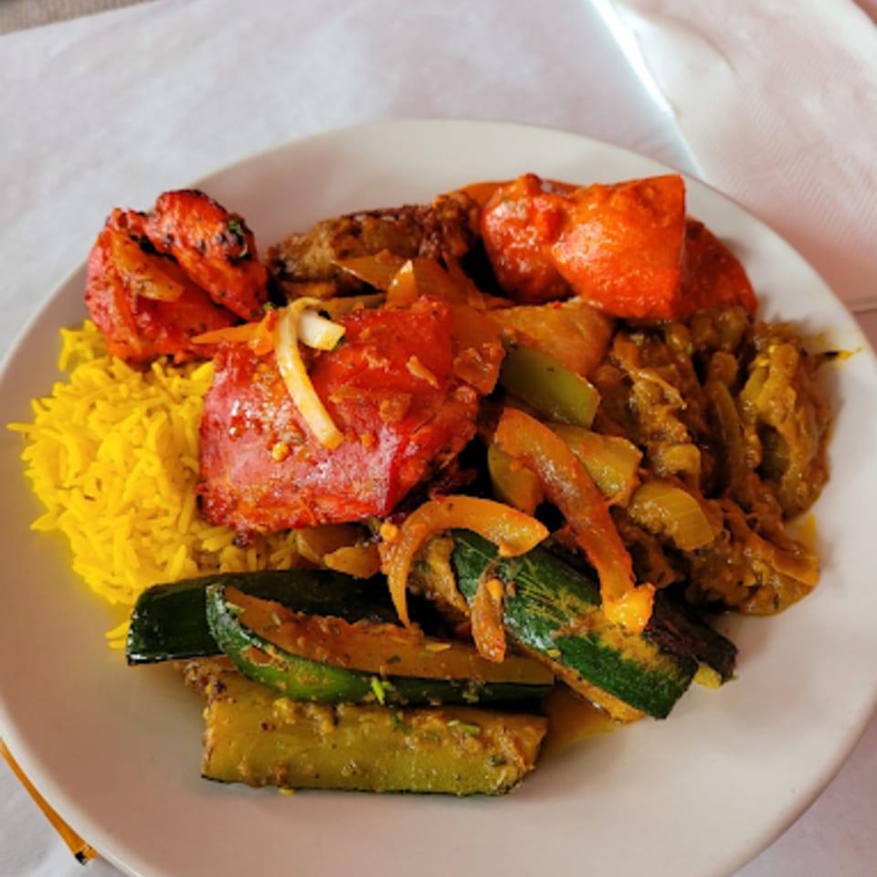 A plate of Indian food with yellow rice, tandoori chicken, and cooked zucchini.