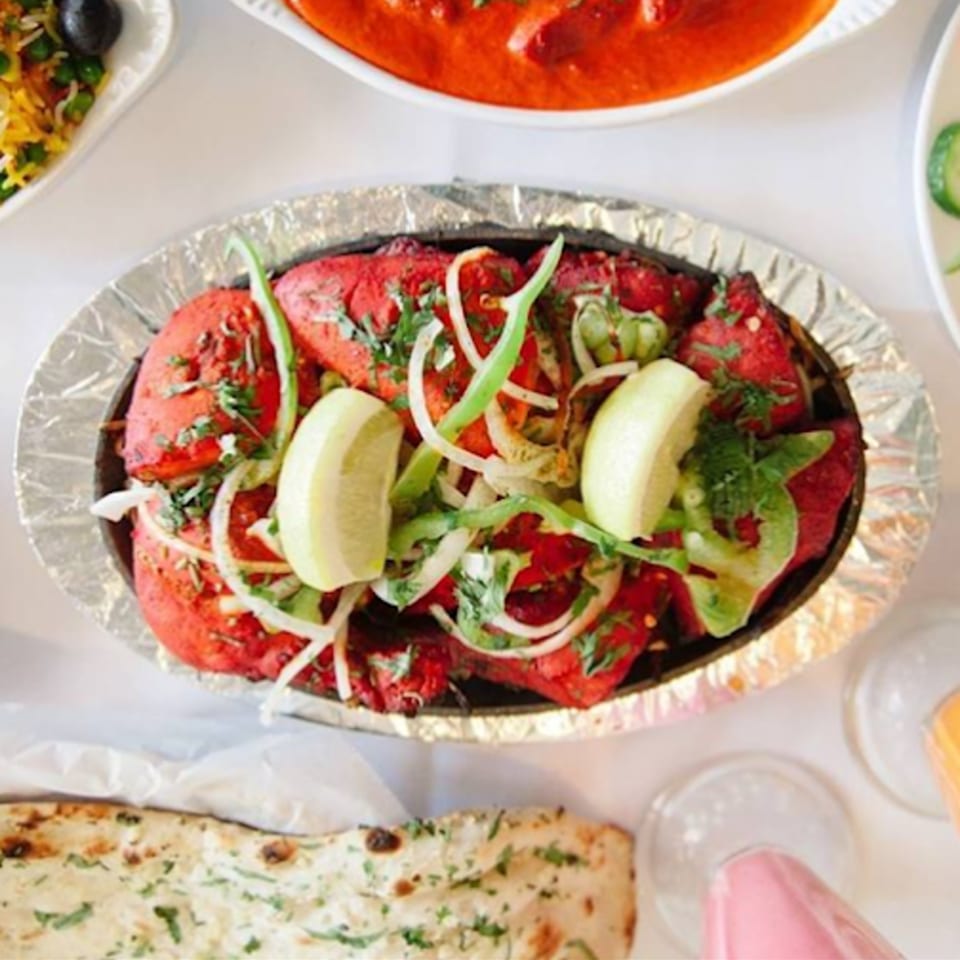 Vibrant red Tandoori chicken, garnished with onions, green peppers, and lemon wedges, in a foil-lined dish.