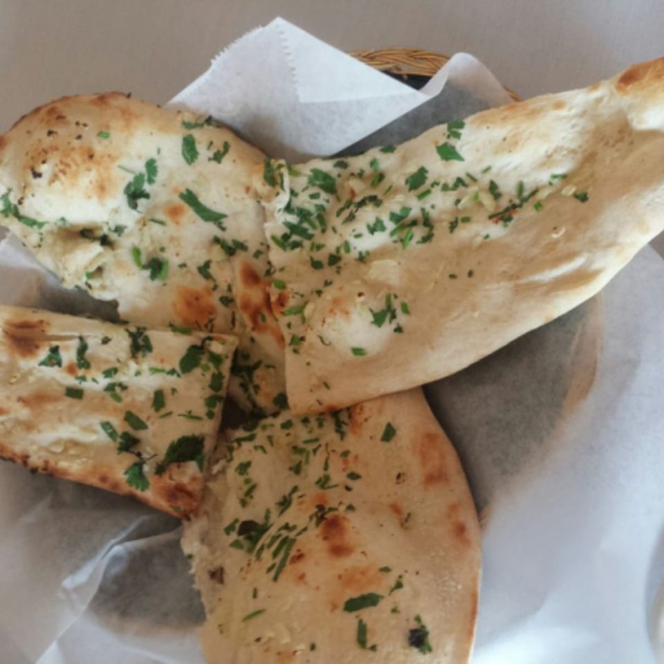 Basket of warm, fluffy naan bread topped with fresh green herbs, from India's Tandoori.